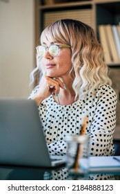 Blonde Businesswoman Working Free At The Office Looking Outside And Thinking With A Smile. Happy Entrepreneur Female People With Glasses. Break From Work Activity Concept. Modern Online Worker