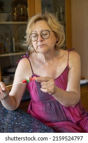 Blonde Caucasian Advanced Age Woman Eating Sweets In The Counter Of Her Vintage Kitchen