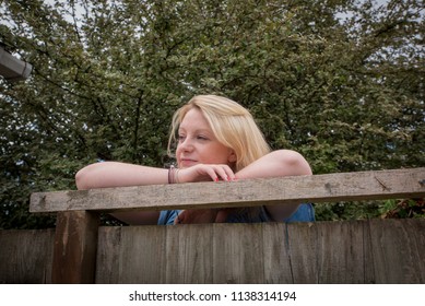 Blonde Caucasian female looking over a wooden fence. 
