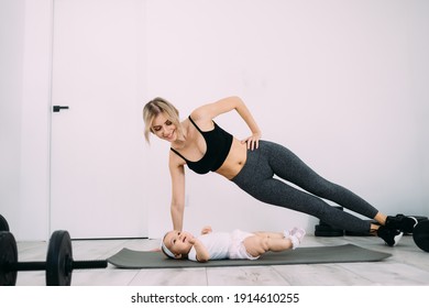 Blonde Caucasian Mother Is Engaged In Fitness With A Small Child On The Floor In The Room. Postpartum Health And Home Recovery Concept. Place For Text.