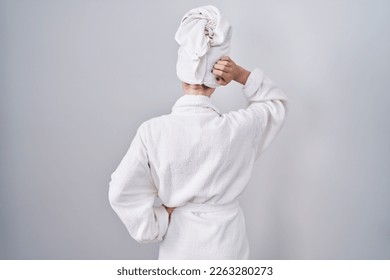 Blonde caucasian woman wearing bathrobe backwards thinking about doubt with hand on head  - Powered by Shutterstock