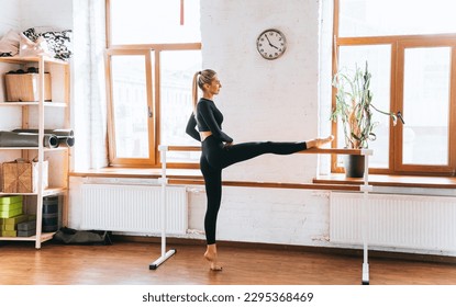 Blonde caucasian young female dancer stretching using ballet bar at fitness class. Fit American blonde girl improving flexibility on sunny morning home. Active people, sport, healthy women. - Powered by Shutterstock