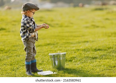 Blonde curly boy standing on a grass and holding a box with a baits for fish