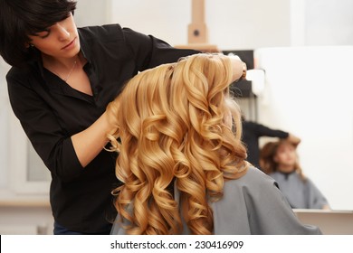 Blonde Curly Hair. Hairdresser Doing Hairstyle For Young Woman In Salon