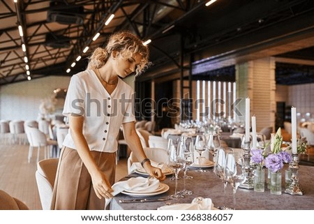 blonde decorator with wavy hair arranging banquet setting on table with floral decor in event hall Stockfoto © 