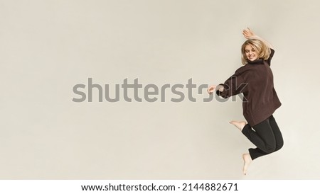 Blonde european girl with short hair in casual clothes jumping with inspirational expression. Active young woman having fun in a beige room. copy space