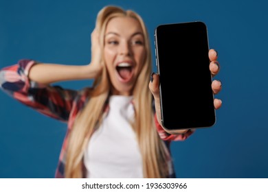 Blonde Excited White Woman Exclaiming While Showing Mobile Phone Isolated Over Blue Background