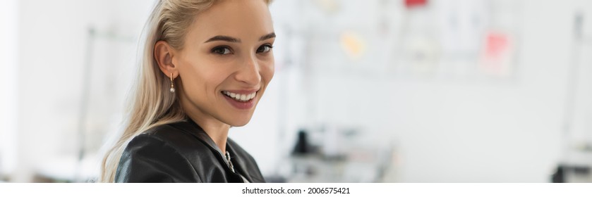 blonde fashion designer smiling at camera in tailor shop, banner