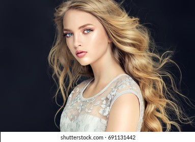 Blonde fashion  girl with long  and   shiny curly hair .  Beautiful  model  in light blue dress with wavy hairstyle .
