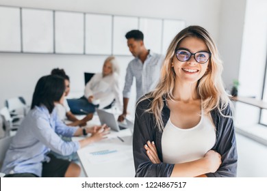 Blonde female executive posing with smile and arms crossed during brainstorm with managers. Indoor portrait of european student spending time in hall with asian and african friends. - Shutterstock ID 1224867517