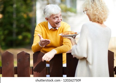 Blonde Female Giving Her Neighbour Piece Of Homemade Apple Pie Over Wooden Fence