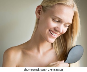 A Blonde Female Model Smiling While Brushing Her Smooth Long Healthy Hair.