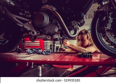 Blonde Female Repairing Motorcycle In A Garage.