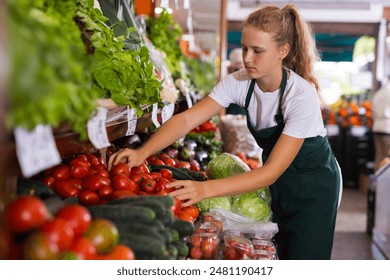 Blonde female seller in uniform working in supermarket at her first job, sorting fresh tomato - Powered by Shutterstock