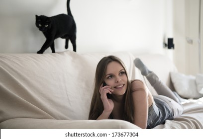 Blonde Girl And Black Cat Stretched On The Couch Talking On Mobile Phone