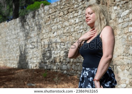 Blonde girl in floral skirt dances in a field, backdrop of a stone wall.