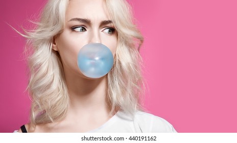 Blonde Girl Inflates A Bubble Of Gum Blue On A Pink Background