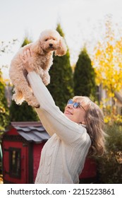 A Blonde Girl Joyfully Throws Up A Cute Toy Poodle Puppy On Her Arm - Love And Friendship Between A Man And A Dog