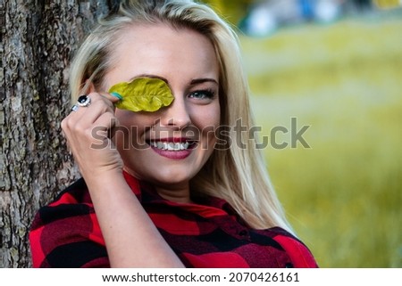 blonde girl leaning her head against a tree, playfully hides one eye behind a leaf, loving nature