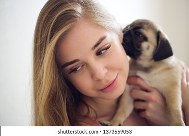 blonde girl with long hair kisses and holds a pug puppy in her arms, high key, gentle toning