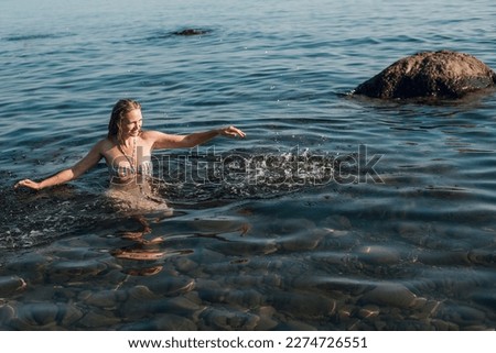 A blonde girl with long hair, in a striped swimsuit, bathes in the ocean, laughs, plays and splashes on a bright sunny day.
