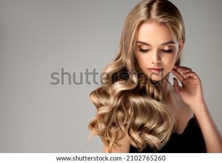 Blonde girl with long  and   shiny wavy hair .  Beautiful  woman model with curly hairstyle .