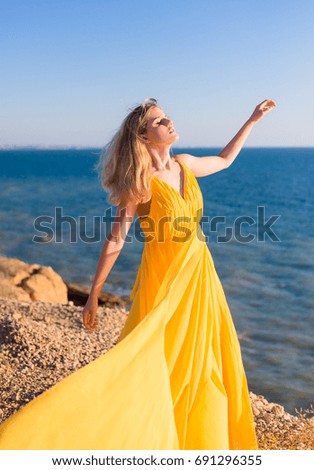 A blonde girl in a long yellow dress on a seashore
