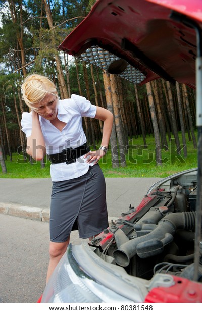 Blonde girl\
looks under the hood of a broken\
car