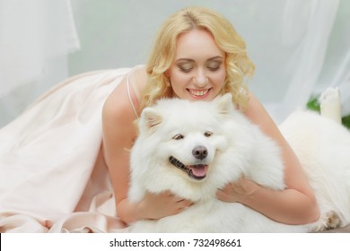 blonde girl is lying outdoors with a white dog in hands - Shutterstock ID 732498661