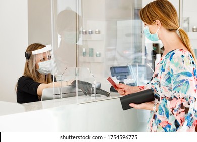 Blonde Girl With Mask Pays At The Checkout With A Credit Card Where The Cashier Is Protected By A Plexiglass Plate And A Visor With Mask