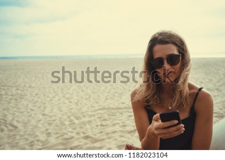 Blonde Girl messaging against a blurred beach background