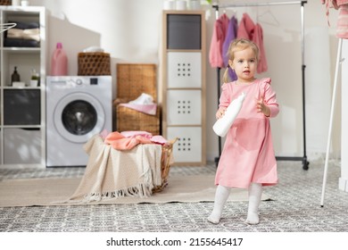 Blonde Girl With Non-beige Eyes Cute Baby In Pink Dress. Girl Plays In Laundry Room With Liquid, Soap Bottle, Help Mom With Household Chores.