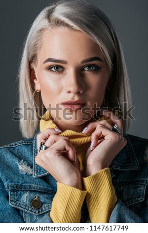 blonde girl posing in yellow turtleneck and jeans jacket, isolated on grey