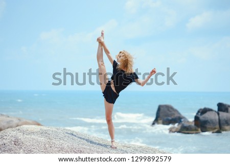 blonde girl practicing yoga on a rock by the beach