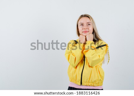  blonde girl propping chin on fists in yellow jacket and looking dreamy. front view. 