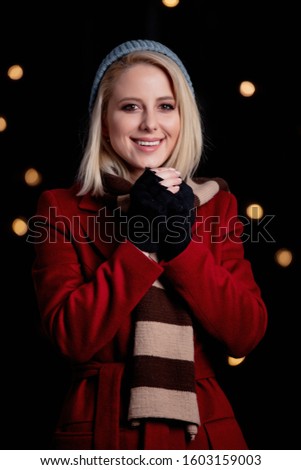 Blonde girl in red coat, and scarf on background with fairy lights