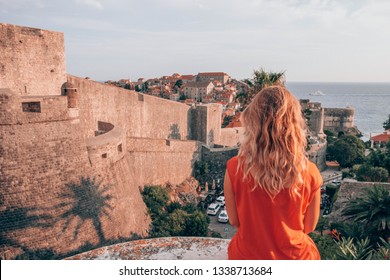 Blonde Girl in a red dress is visiting game of thrones location in Dubrovnik, Croatia. Woman traveller in front of famous travel destination. Free blonde enjoying vacation. Europe Lifestyle. 