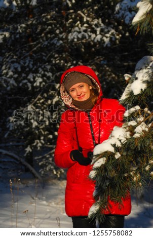 Blonde girl in red scarf and coat walking at park on winter day.