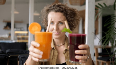 Blonde girl showing to the camera glasses of natural organic carrot and beetroot juices with paper straws. Plant based cold refreshing drinks.