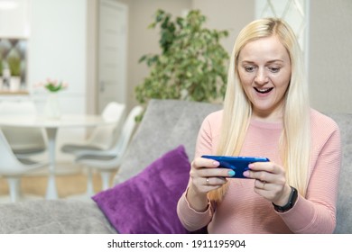 Blonde Mädchen sitzen auf dem Sofa und spielen das Telefon. hohe Qualität