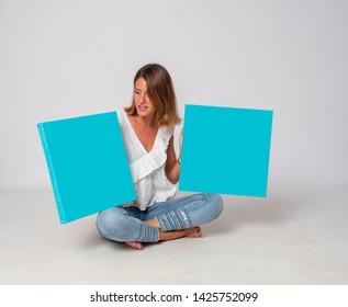 Blonde girl sitting on the floor with white background holding blue pictures to put your text - Shutterstock ID 1425752099