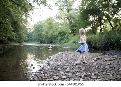 Blonde Girl Skipping Rocks At A Creek