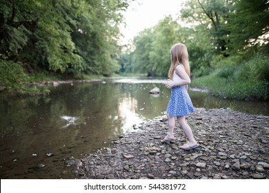 Blonde Girl Skipping Rocks At A Creek