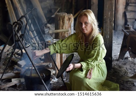 Blonde girl in vintage viking clothing prepares food in a cauldron on a fire