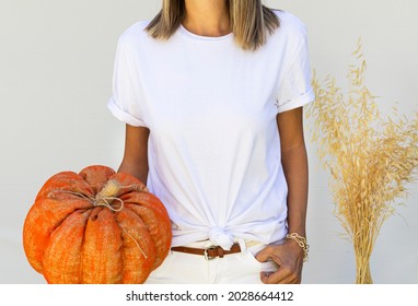 Blonde Girl Wearing Blank White T Shirt And Holding Orange Pumpkin With Urban Clothing. Halloween Shirt Mock Up. Your Design Template