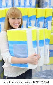 Blonde Girl Wearing White Shirt Holds Big Pack Of Toilet Paper In Shop; Shallow Depth Of Field