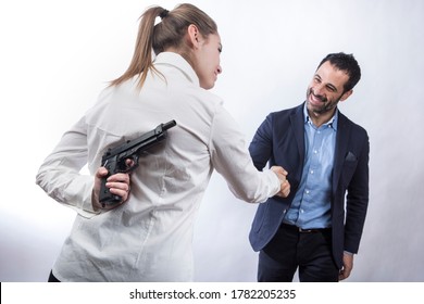 blonde girl in white shirt holds a gun in her hand while shaking hands with a dark-haired man dressed in jacket and shirt, isolated on white background