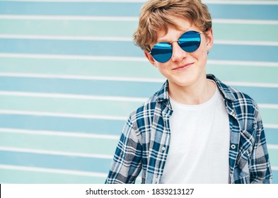 Blonde Hair 12 Year Old Caucasian Teenager Boy Fashion Portrait Dressed White T-shirt With Checkered Shirt In Blue Sunglasses With Turquoise Blue Background Wall Background. Teens Fashion Concept.