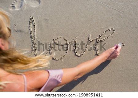 Blonde hair young woman writting on sand "love" inscription. Girl drawing a heart on the sand at sunset in a summer love concept. A girl writing with sands. 