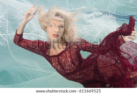 Blonde haired model posing underwater in a red frilly dress.